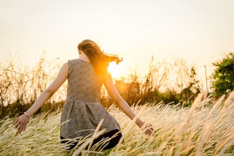 Femme les bras ouverts dans un champ doré au coucher du soleil, symbolisant la libération des émotions et le lâcher-prise