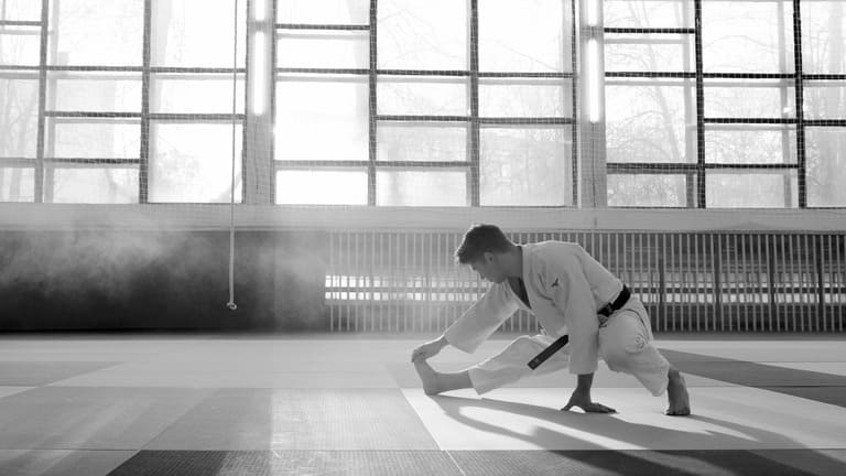 udoka ceinture noire s'étirant seul sur un tatami, symbolisant la concentration et la préparation mentale