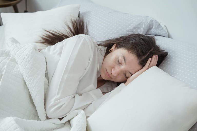 Femme dormant paisiblement dans un lit blanc symbolisant un sommeil profond et réparateur grâce à l'hypnose