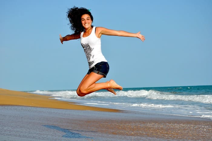 Femme souriante sautant sur une plage pour illustrer le bien-être retrouvé après l'arrêt du tabac