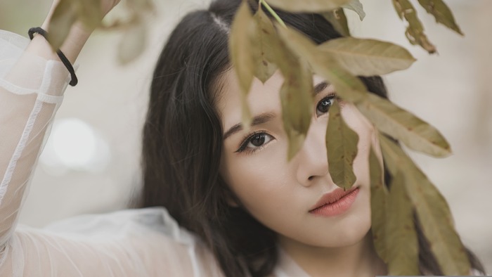 Jeune femme au regard discret derrière des feuilles illustrant la peur du regard des autres, le manque de confiance en soi et la peur du jugement.