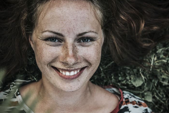 Jeune femme allongée dans l'herbe, souriante et détendue, illustrant une approche globale du bien-être et de la sophrologie.