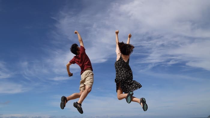 Deux personnes sautent de joie sous un ciel bleu, illustrant la liberté de prendre soin de soi sans culpabilité et d'écouter ses besoins.