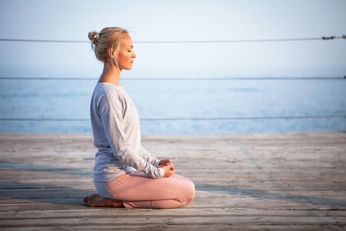 Femme pratiquant un exercice de respiration et de relaxation en bord de mer, illustrant une séance de sophrologie.