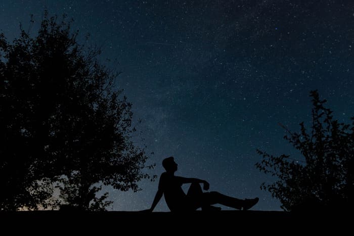 Personne assise sous un ciel étoilé prenant du recul face à ses pensées