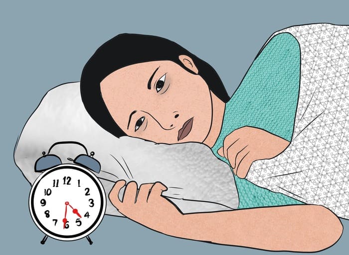 Femme éveillée au lit illustrant la rumination mentale le soir et les pensées qui tournent en boucle avant de dormir