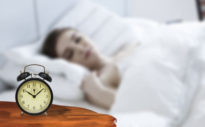 Réveil près du lit illustrant la rumination mentale le soir et les difficultés à apaiser ses pensées avant de dormir