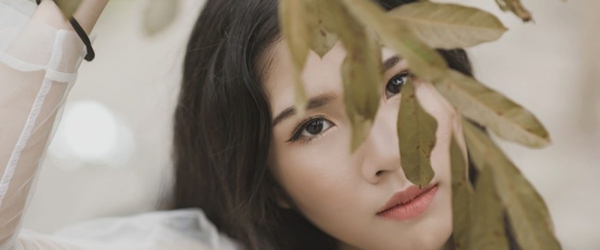 Jeune femme au regard discret derrière des feuilles illustrant la peur du regard des autres, le manque de confiance en soi et la peur du jugement.