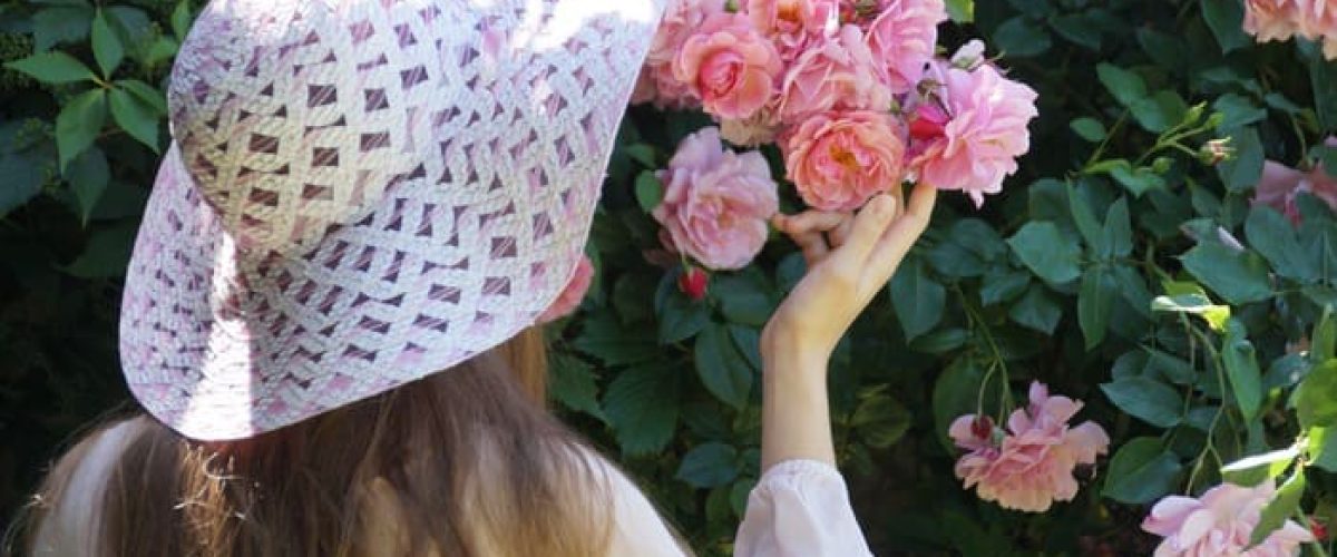 Une personne contemple et touche délicatement des roses dans un jardin, symbole du bien-être, de la sérénité et du fait de prendre soin de soi sans culpabilité.